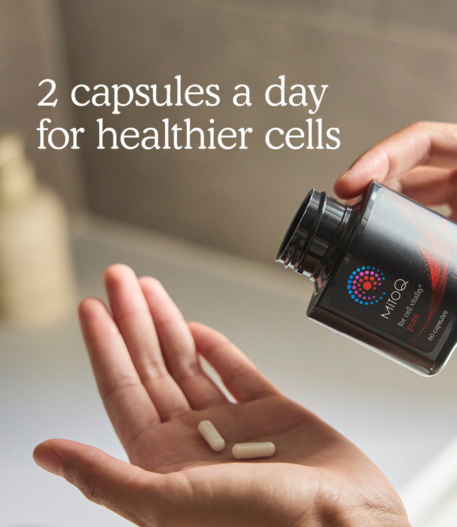 A person holds an open black supplement bottle while pouring two white capsules into their open palm. White text on the image reads '2 capsules a day for healthier cells.