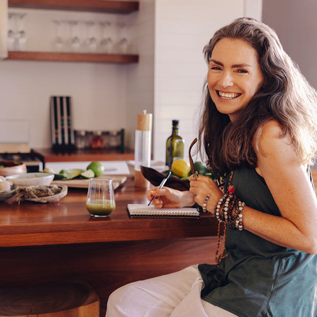 Woman sitting at a kitchen counter with a glass of juice, smiling.